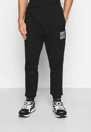 Zwarte sweatpants met een aansluitende Manchette, voorzien van een textuur rectangular logo patch, gemaakt van zachte stof. Gepaarde met zwart-witte sneakers.