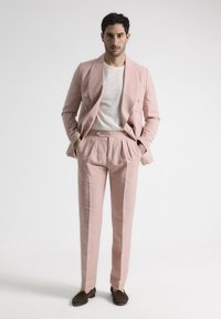 Conjunto de lino rosa claro con chaleco de doble botonadura, pantalones plisados y zapatos marrones tipo slip-on, con una camiseta blanca minimalista debajo.