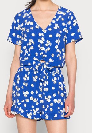 Blauwe tweedelige outfit met witte madeliefjesprint, korte mouwen, top met knopen aan de voorkant, gestrikte taille en short met ruches aan de zoom.