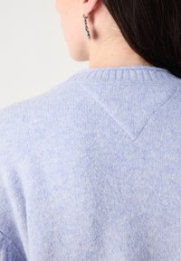 Lichtblauwe trui met een geribde halslijn, textuurstof en een driehoekige naaddetail op de achterkant. Zacht, warm materiaal duidelijk zichtbaar.