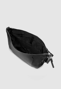 Schwarze Lederhandtasche mit Reißverschluss, innen mit Innenfutter im Markenlogo-Muster und abnehmbarem Riemen. Strukturierte Oberfläche.