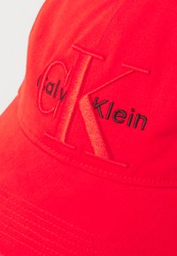 Rode katoenen pet met geborduurd zwart "Calvin Klein" logo. Gestructureerd ontwerp met een gebogen rand en textiele stof.