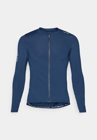 Maillot de cyclisme à manches longues bleu marine avec fermeture éclair à l'avant, détail de logo sur l'épaule et texte contrastant en bas de l'ourlet. Texture de tissu lisse.