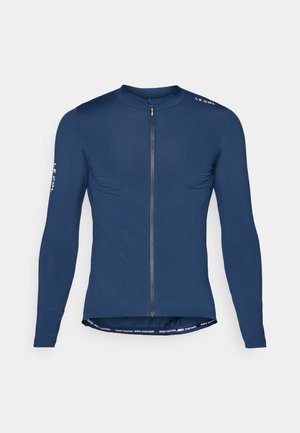 Maillot de cyclisme à manches longues bleu marine avec fermeture éclair à l'avant, détail de logo sur l'épaule et texte contrastant en bas de l'ourlet. Texture de tissu lisse.