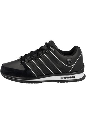 Baskets K-Swiss noires avec lacets noirs, accents blancs, cinq bandes latérales et une semelle blanche avec le nom de la marque sur le côté.