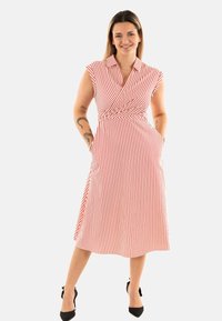 Czerwona i biała w paski sukienka kopertowa z krótkim rękawem, kieszeniami i dopasowaną talią, sięgająca do połowy łydki. Czarne szpilki dopełniają całość.