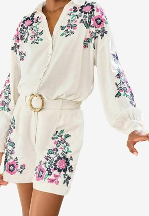 Wit blouse- en shortset met knopen, versierd met roze, zwarte en groene bloemenborduurwerk, voorzien van een ronde, geweven riemgesp in de taille.