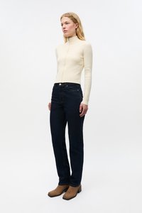 Kremfarget ribbestrikket turtleneck-genser, mørkeblå denimjeans og brune semskede ankelstøvler. Enkel, tettsittende design med teksturert stoff.