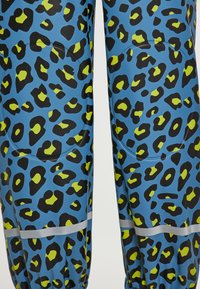 Leggings blu con un motivo leopardato nero e verde lime, dotati di una striscia riflettente argento e di una texture liscia ed elastica.
