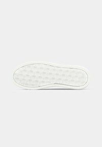 Witte sneakerzool gezien vanaf de onderkant, met een tegelpatroon en herhaalde "CK"-logo's.