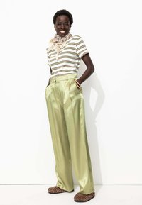 Chemise à rayures à manches courtes, trousers taille haute en satin vert, chaussures à imprimé animal et une légère écharpe à motifs. Textures lisses et coupe décontractée.