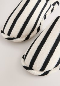 Paire de chaussons en tissu doux avec des rayures verticales noires et blanches, bout rond et texture rembourrée sur une surface claire.