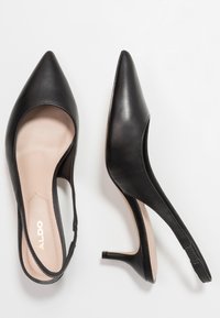 Czarne skórzane sandały na obcasie typu slingshot z ostrym noskiem, niskim szpilkowym obcasem i jasnobrązową wkładką. Elegancki design o gładkiej fakturze.