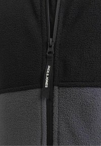 Giacca a zip in pile nera e grigia con finitura testurizzata, colori a contrasto e una zip con tirazip brandizzato con l'iscrizione "JACK & JONES".