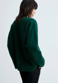 Grön, fluffig oversized tröja med rund halsringning och sänkta axelsömmar. Bakdelen har en avslappnad passform, kombinerad med svarta byxor.