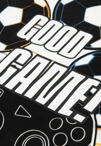 Camiseta con gran texto en blanco y negro "¡BUEN JUEGO!" superpuesto sobre gráficos de un balón de fútbol, con un diseño de controlador de videojuego en blanco y negro.