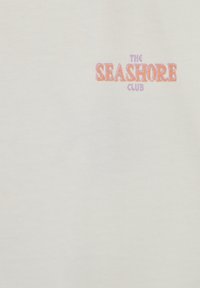 Tissu blanc avec petit texte "THE SEASHORE CLUB" en violet et orange en haut à droite.