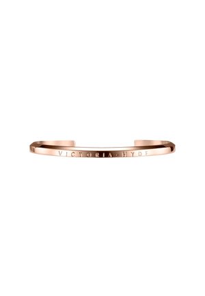 Brazalete de metal en oro rosa grabado con "VICTORIA HYDE" en la parte frontal, abierto y de diseño minimalista.