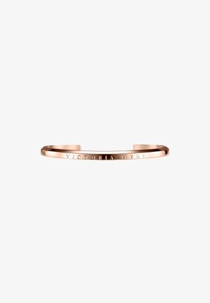 Bracelet manchette en métal rose doré gravé de "VICTORIA HYDE" sur le devant, ouvert et au design minimaliste.