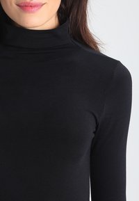 Svart, langermet turtleneck-genser laget av stretchy stoff, med en slim fit-design og glatt tekstur, med høy hals.