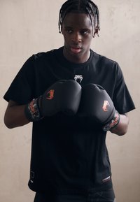 Černé sportovní tričko s hadím logem, spárované s černými boxerskými rukavicemi s oranžovými akcenty a vzorovaným zápěstním popruhem.