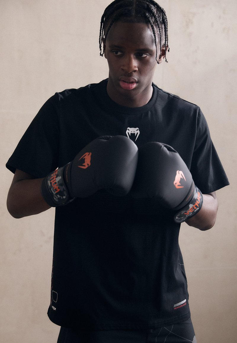 Černé sportovní tričko s hadím logem, spárované s černými boxerskými rukavicemi s oranžovými akcenty a vzorovaným zápěstním popruhem.