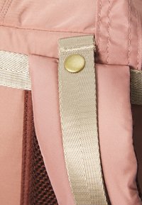 Détail d'un sac en tissu rose avec un fermoir en métal doré et une anse tissée beige. La texture est lisse avec un léger éclat.