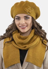Senapsgul stickad basker med blomdekorationer, tillsammans med en matchande scarf med ribbade kanter. Mjuk textur, varm design.