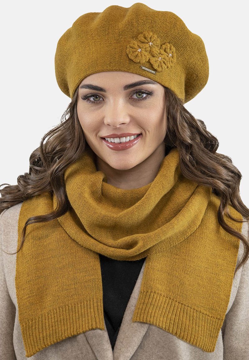 Senapsgul stickad basker med blomdekorationer, tillsammans med en matchande scarf med ribbade kanter. Mjuk textur, varm design.