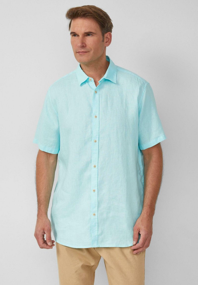 Camicia azzurra chiara a maniche corte con bottoni, realizzata in un tessuto leggero, con colletto a punte e bottoni beige. Texture liscia.