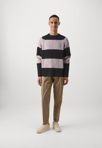Pulover în dungi, de culoare roz deschis și negru, cu textură tricotată, croială relaxată, guler rotund. Asortat cu pantaloni bej și adidași de culoare deschisă.