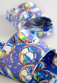 Blå tofflor med ett livligt fotbollsmönster och glänsande accenter, tillverkade av mjukt syntetiskt material. Kurvad design med breda remmar.