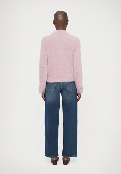 Chlpatý ružový kardigán s šálom, skombinovaný s širokými tmavomodrými džínami. Oblečenie má uvoľnený strih a jemnú textúru.