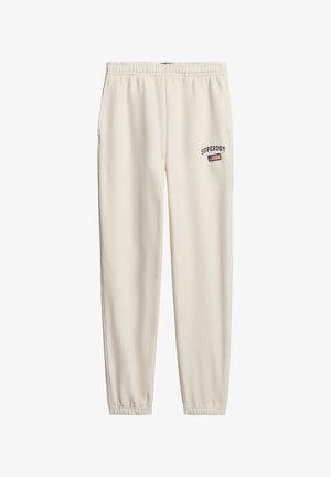 Pantaloni jogger color crema con un elastico in vita. Presentano il logo "SUPERDRY" e una toppa con la bandiera vicino all'anca. Tessuto morbido, design con gamba affusolata.