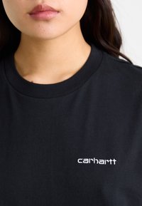 Must läikiv must puuvillane T-särk, millel on ümar kaelus ja lühikesed varrukad, vasakul rinnal on valge "carhartt" emblem.