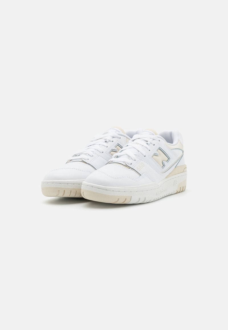 Sneakers bianchi con tomaia in pelle liscia, dettagli in beige chiaro e suola testurizzata. Tra le caratteristiche ci sono i lacci e un dettaglio di branding sul lato.
