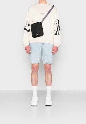 Personne portant un sweatshirt blanc Calvin Klein, un short en denim bleu clair, des chaussettes blanches, des baskets blanches et un sac en bandoulière noir.