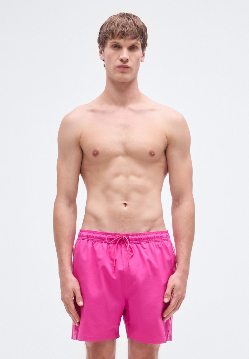 Φωτεινά ροζ μαγιό βερμούδα με ελαστική ζώνη μέσης, μπροστινό κορδόνι και πλαϊνές τσέπες. Ομαλή υφή και μήκος μέχρι το γόνατο.