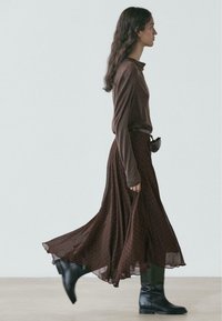 Brown long-sleeve top paired with a flowing, dotted brown skirt. The outfit is completed with knee-high black boots and a belt.