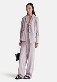 Jasnofioletowy garnitur z kordury, składający się z marynarki z dwoma guzikami i kieszeniami naszytymi, w połączeniu z szerokimi spodniami. Czerń torby i masywne sneakersy.
