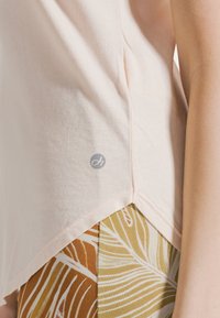 Camiseta de manga corta color rosa pálido con dobladillo curvado, hecha de tela de algodón suave. Cuenta con un pequeño logo cerca del dobladillo y se combina con pantalones estampados.