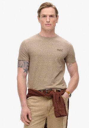 Brun kortærmet t-shirt med et tekstureret mønster, rund hals og et lille broderet logo. Sammen med beige bukser og en brun skjorte knyttet om livet.