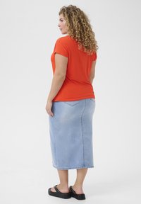 Camiseta naranja de manga corta combinada con una falda midi de mezclilla azul claro, con corte recto y un leve desgaste, complementada con sandalias negras.