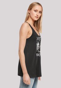 Schwarzes Tanktop mit breiten Trägern und grafischem Design. Der Stoff hat eine glatte Textur und eine lässige Passform, getragen über hellblauen Jeans.