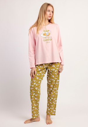 Mujer con camiseta de manga larga rosa con un perro y el texto "Una siesta siempre es una buena idea" y pantalones verde oliva con estampado de perro dormido. Descalza.