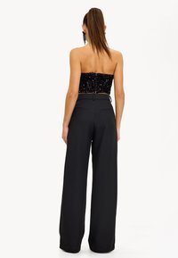Top corto negro con lentejuelas y diseño sin tirantes, combinado con pantalones de pierna ancha negros de cintura alta con corte sastre y bolsillos en la parte posterior.
