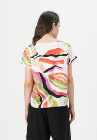 Bluză cu mânecă scurtă dintr-un material ușor, având un model abstract colorat cu linii roșii, verzi, roz și negre pe un fundal alb.