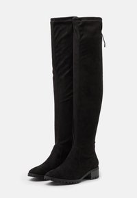 Botas negras por encima de la rodilla realizadas en un material similar al ante, con una superficie texturizada, puntera redondeada y tacón bajo, además de cremallera lateral.