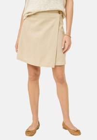Beige insvept kjol tillverkad av texturerad tyg, med en knapprad på sidan och en slät yta. Kombinerad med ljusbruna vävda skor.