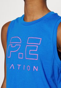 Top sin mangas de algodón azul que presenta un gran texto en rosa que dice "P.E NATION" en el pecho. Textura suave, diseño casual.